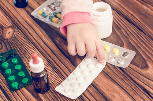 Children's hands with medicines on a wooden table. A small child